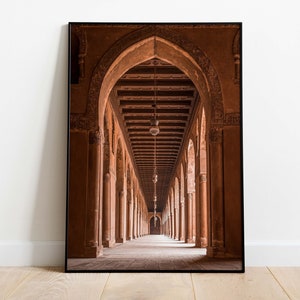 Może przedstawiać: Długi, wąski korytarz z łukowymi sufitami i kolumnami. Ściany i kolumny są w ciepłym, czerwonawobrązowym kolorze. Światło wpada z końca korytarza, tworząc jasny punkt w środku.