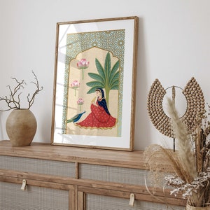 May include: A framed illustration of a woman in a red and blue dress sitting under a palm tree with a peacock. The background is a blue and gold geometric pattern.
