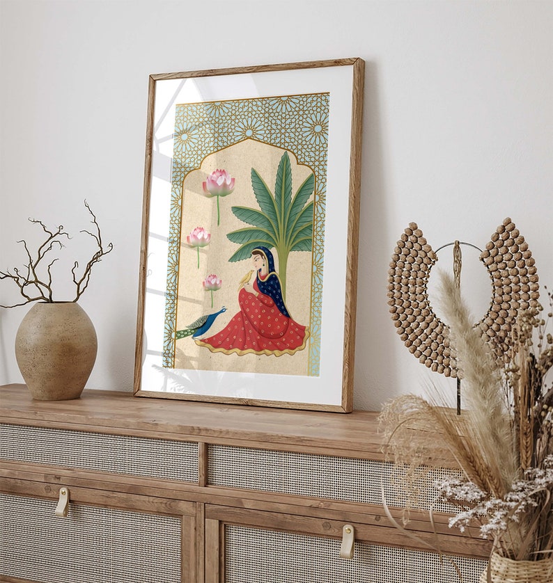 May include: A framed illustration of a woman in a red and blue dress sitting under a palm tree with a peacock. The background is a blue and gold geometric pattern.