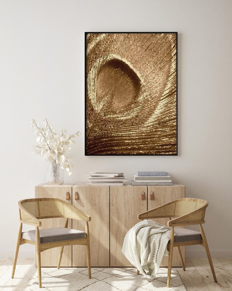 May include: A framed abstract print with a swirling pattern in shades of brown and gold. The print is hanging on a white wall above a wooden cabinet with two chairs.
