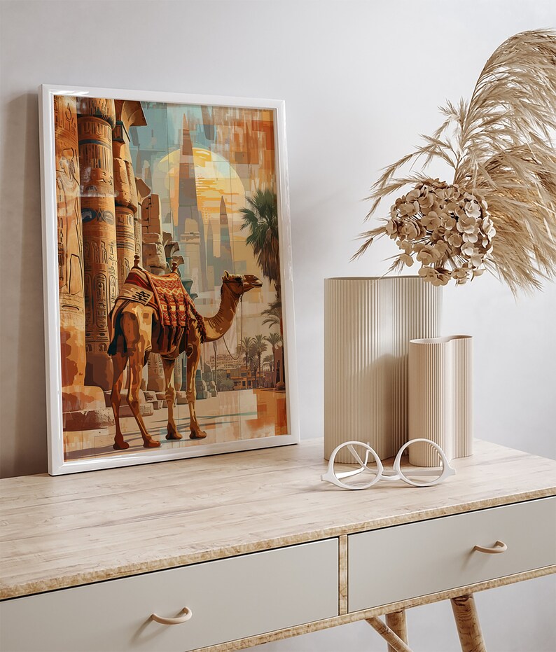 May include: A framed painting of a camel standing in front of an ancient Egyptian temple. The camel is brown with a saddle and is looking to the right. The temple is made of stone and has tall columns. The painting is set against a background of a sunset.