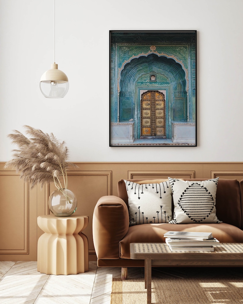 May include: A framed print of an ornate teal and gold door. The door is set within an arched doorway with intricate carvings. The print is displayed above a brown sofa with decorative pillows and a wooden coffee table.