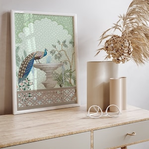 May include: A framed print of a peacock standing on a fountain with a green and white geometric pattern background. The print is in a white frame and is sitting on a wooden table with two drawers.