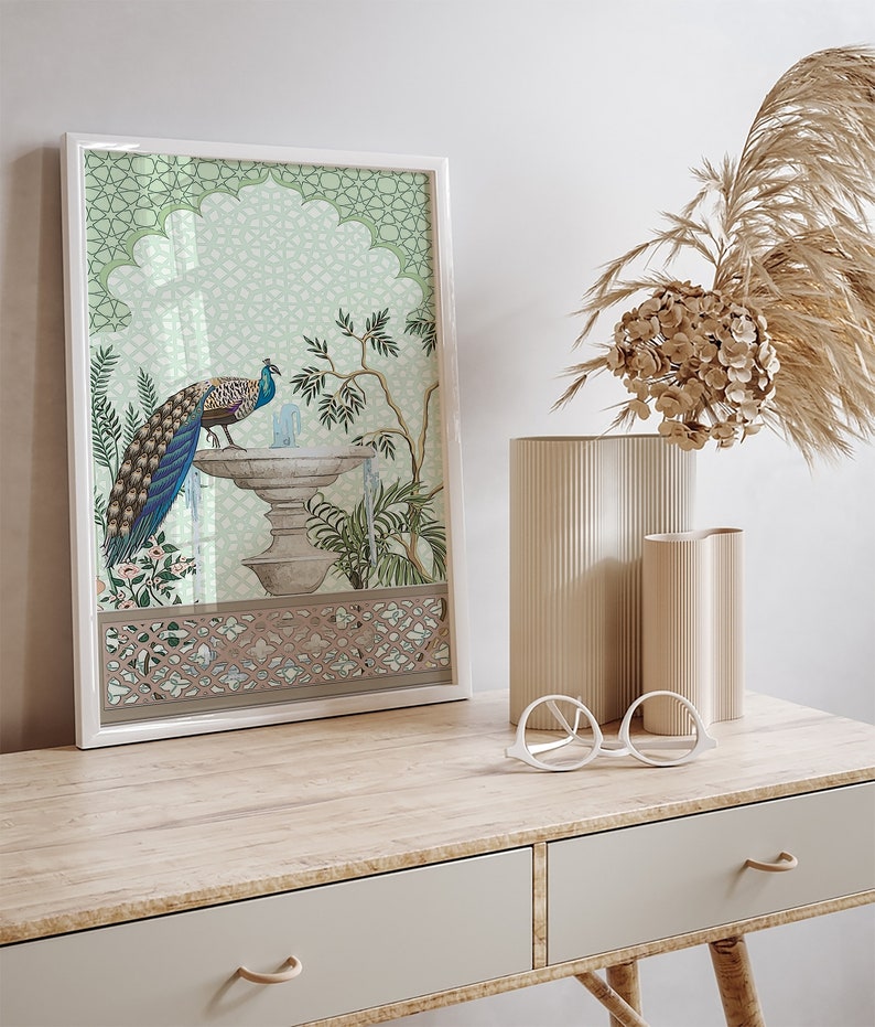 May include: A framed print of a peacock standing on a fountain with a green and white geometric pattern background. The print is in a white frame and is sitting on a wooden table with two drawers.