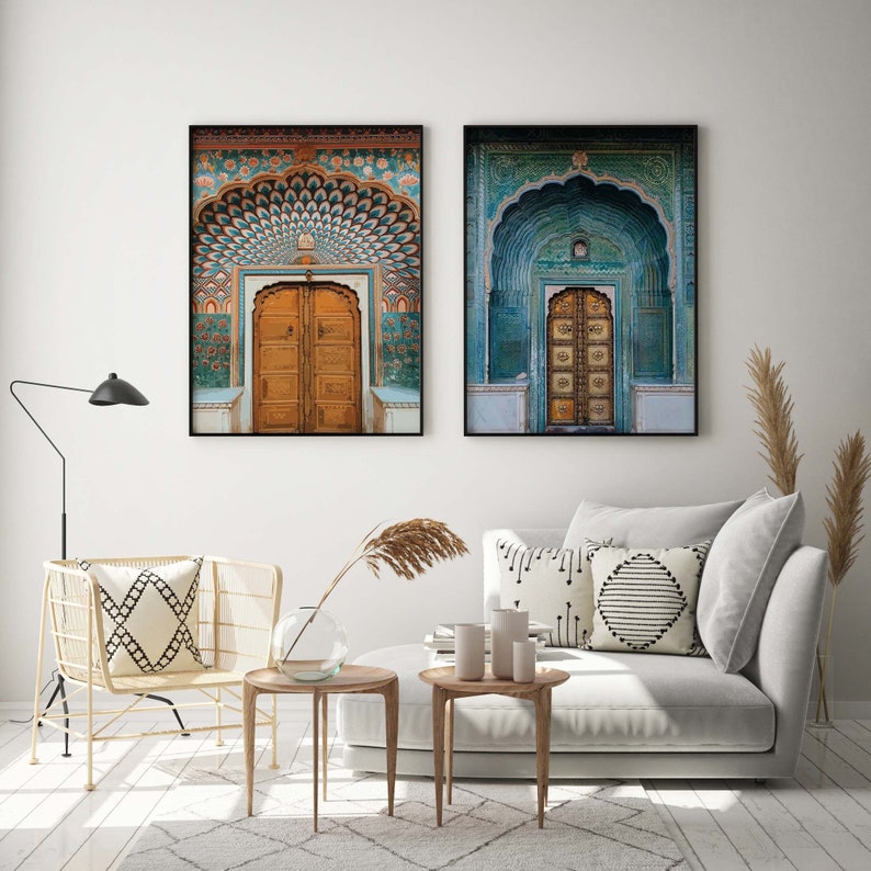 May include: Two framed prints of ornate Indian doors. One features a brown door with a teal and orange archway, the other a gold door within a teal arch. The prints hang above a white sofa and wooden side tables.