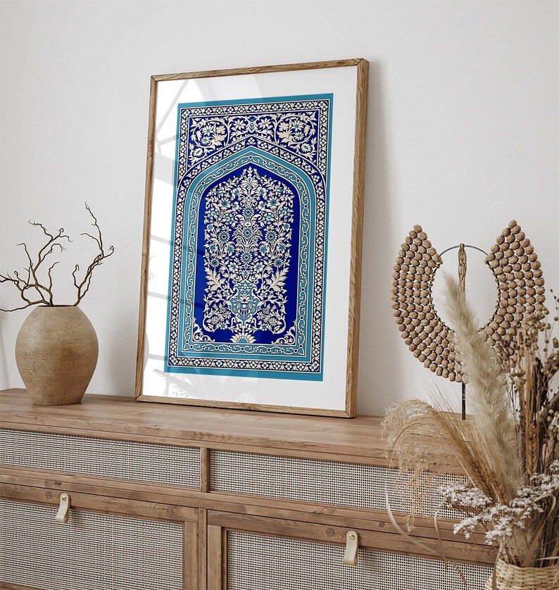 Puede incluir: Una impresi&oacute;n enmarcada de una alfombra azul y blanca con intrincados dise&ntilde;os florales. La alfombra est&aacute; enmarcada en un marco de madera natural y est&aacute; colgada en una pared blanca sobre un armario de madera.