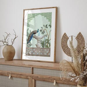 May include: A framed print of a peacock standing on a fountain with a green and blue patterned background. The fountain is surrounded by plants and flowers. The frame is made of wood and has a light brown finish.