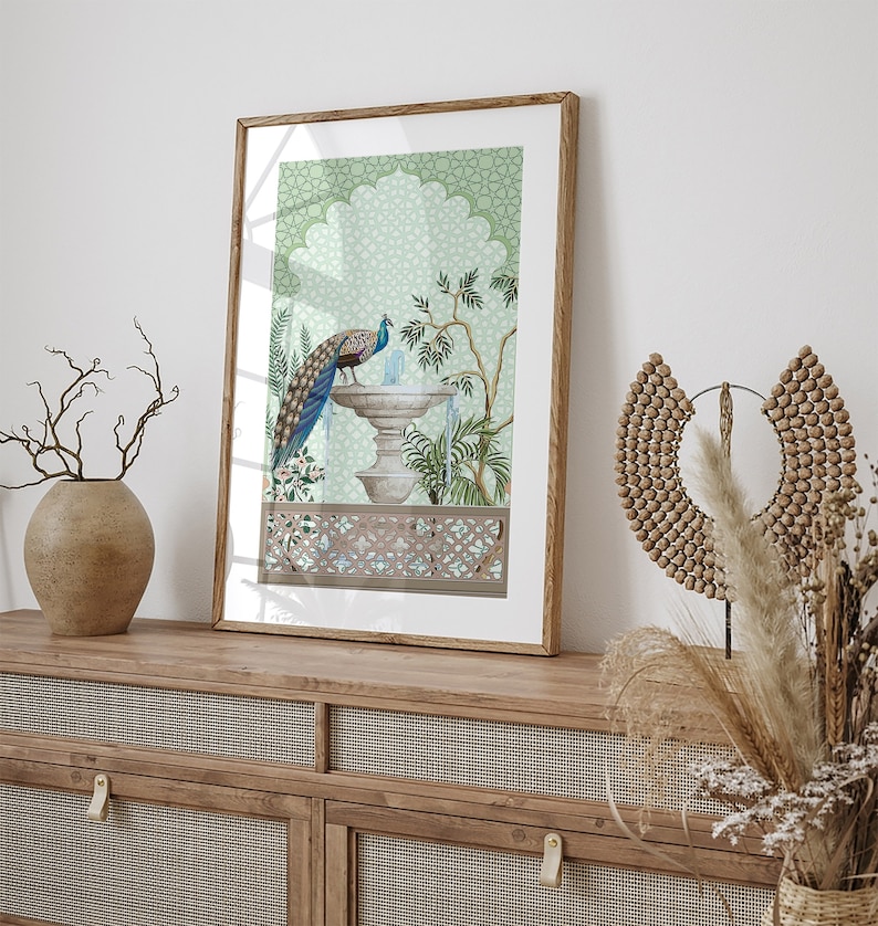 May include: A framed print of a peacock standing on a fountain with a green and blue patterned background. The fountain is surrounded by plants and flowers. The frame is made of wood and has a light brown finish.