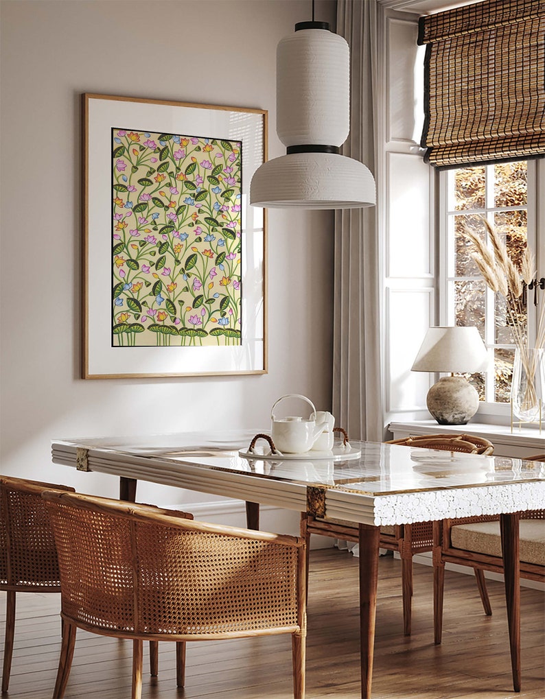 May include: A dining room with a white table and chairs with woven cane seats. The table has a glass top and a white ceramic teapot and cups on it. A framed print of a floral pattern hangs on the wall behind the table. A white pendant light hangs above the table.