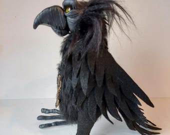 May include: A black crow puppet with a detailed face and feathered wings. The crow has a steampunk-inspired design with a key and gears on its chest.