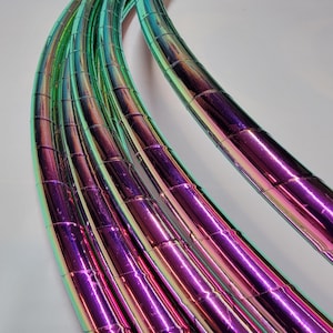 Könnte beinhalten: Mehrere regenbogenfarbene Hula-Hoop-Reifen in Grün- und Lilatönen. Die Reifen sind aus flexiblem Material gefertigt und haben eine glänzende, reflektierende Oberfläche.