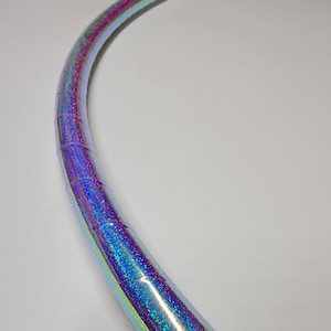 Puede incluir: Primer plano de un aro azul y morado iridiscente con purpurina. El aro es de plástico y es flexible.