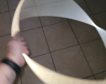May include: A person is holding a white wooden hoop, spinning it in a circle. The hoop is blurred due to the motion of the spin.