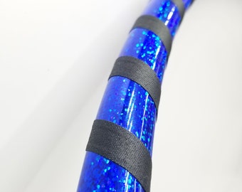 Può includere: Un cerchio blu e nero con glitter iridescente. Il cerchio è fatto di plastica e ha un'avvolgimento di nastro nero.
