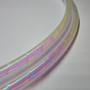 Op de afbeelding: Twee iriserende witte plastic hoelahoepringen met een regenboogkleurige glans. De ringen liggen op elkaar.