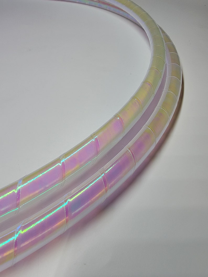 Op de afbeelding: Twee iriserende witte plastic hoelahoepringen met een regenboogkleurige glans. De ringen liggen op elkaar.