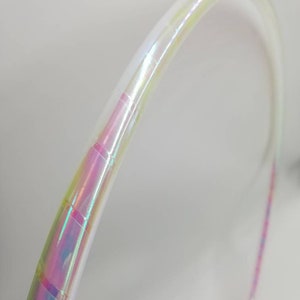 Op de afbeelding: Een witte, iriserende hoepel met een regenboogkleurige, iriserende tape-wikkeling. De hoepel is gemaakt van plastic en is flexibel.