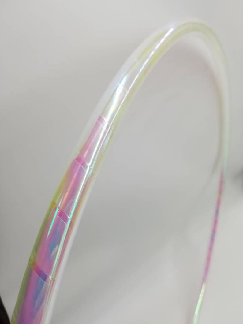 Op de afbeelding: Een witte, iriserende hoepel met een regenboogkleurige, iriserende tape-wikkeling. De hoepel is gemaakt van plastic en is flexibel.