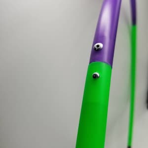 May include: A purple and green hula hoop with silver metal accents. The hoop is made of plastic and is flexible.