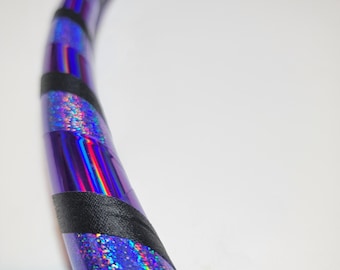 Può includere: Un cerchio viola e nero con glitter iridescente. Il cerchio è fatto di plastica e ha un design a nastro nero.