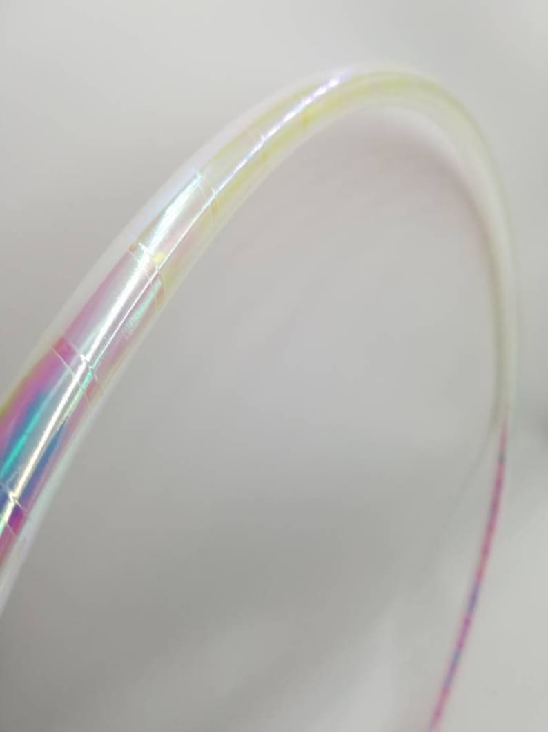 Op de afbeelding: Een witte, iriserende hoepel met een roze en blauwe streep. De hoepel is gemaakt van plastic en is flexibel.