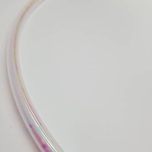 Op de afbeelding: Een transparante, iriserende hoepel met een regenboogkleurige glans. De hoepel is flexibel en gemaakt van plastic.