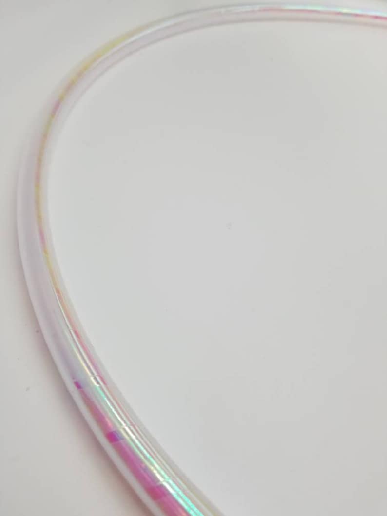 Op de afbeelding: Een transparante, iriserende hoepel met een regenboogkleurige glans. De hoepel is flexibel en gemaakt van plastic.