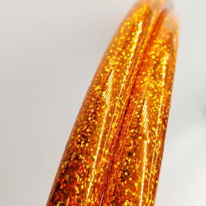 Puede incluir: Dos aros de hula de purpurina naranja, vista cercana de los aros que muestran la textura de la purpurina.