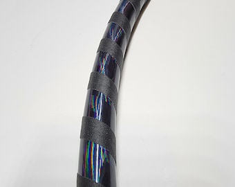 Può includere: Un cerchio nero con nastro iridescente avvolto attorno. Il nastro è nero con un bagliore arcobaleno.