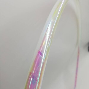 Op de afbeelding: Een witte hoepel met iriserende tape eromheen gewikkeld. De tape heeft een regenboog effect met roze, blauwe en groene kleuren.