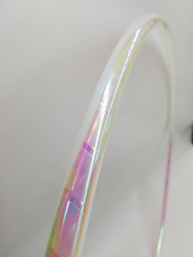 Op de afbeelding: Een witte hoepel met iriserende tape eromheen gewikkeld. De tape heeft een regenboog effect met roze, blauwe en groene kleuren.