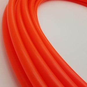 Puede incluir: Primer plano de un aro de plástico naranja brillante, mostrando la superficie lisa y brillante y la forma en que la luz se refleja en el material.