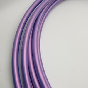 May include: Curved section of a purple hula hoop, with a metallic sheen. The hoop is a vibrant shade of lavender, with subtle highlights. The smooth, rounded tubing is arranged in parallel lines, suggesting a flexible design. The background is plain white.