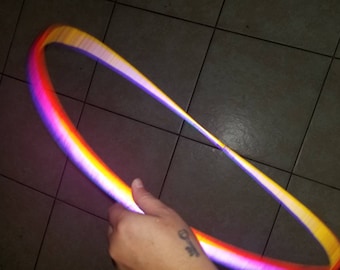 May include: A rainbow-colored plastic hoop with a gradient of purple, blue, yellow, and orange. The hoop is being held by a hand.