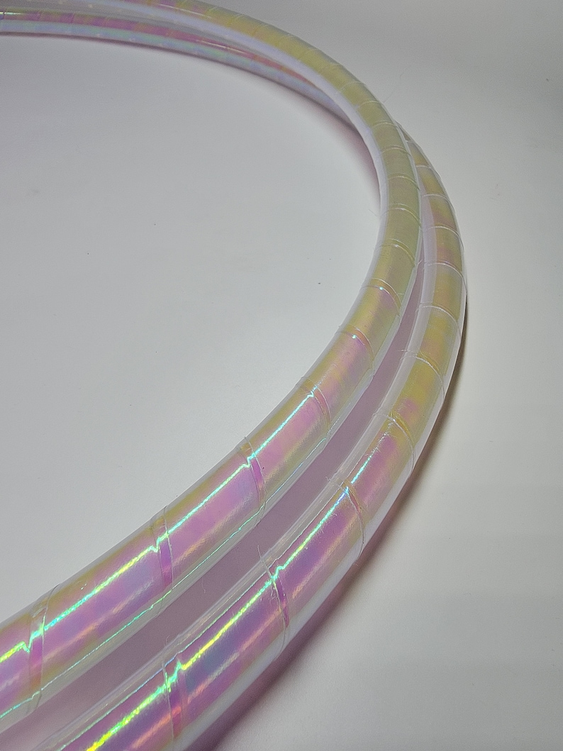 Op de afbeelding: Twee iriserende witte hoelahoepringen met een regenboogkleurige glans. De ringen liggen op elkaar.