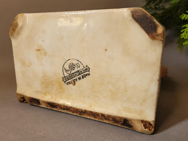 Puede incluir: Objeto de cer&aacute;mica color crema con forma rectangular, que muestra signos de edad y desgaste. La base y los bordes presentan decoloraci&oacute;n marr&oacute;n. La parte inferior tiene un sello negro que dice "MADE IN AUSTRIA WILHELMSBURG".