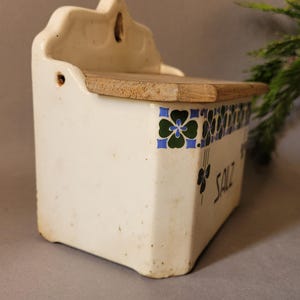Puede incluir: Salero antiguo de cer&aacute;mica blanca con tapa de madera. La caja presenta un dise&ntilde;o floral en azul, verde y negro. La palabra "SALT" est&aacute; escrita en negro en el lateral. Un art&iacute;culo de decoraci&oacute;n de cocina vintage.