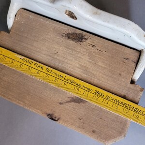 Puede incluir: Una tabla de cortar de madera con un borde de cer&aacute;mica blanca. Una regla amarilla con marcas y texto en negro est&aacute; colocada sobre la tabla. La regla dice "FRANZ FUHL Schmiede Landmaschinen 2803 SCHWARZENBACH".