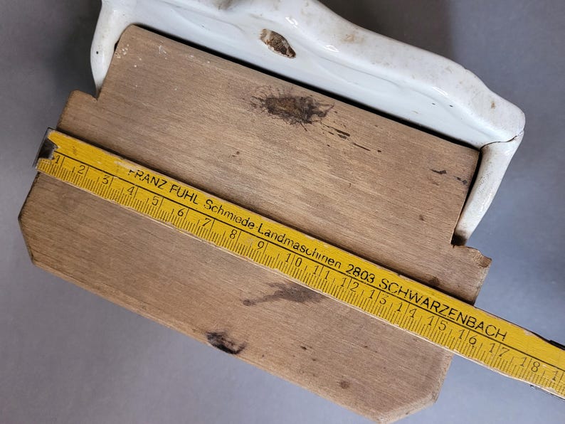 Puede incluir: Una tabla de cortar de madera con un borde de cer&aacute;mica blanca. Una regla amarilla con marcas y texto en negro est&aacute; colocada sobre la tabla. La regla dice "FRANZ FUHL Schmiede Landmaschinen 2803 SCHWARZENBACH".