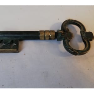 Può includere: Un apribottiglie vintage in ottone a forma di chiave, con una patina verde. L'apribottiglie ha un manico decorativo e un cavatappi.