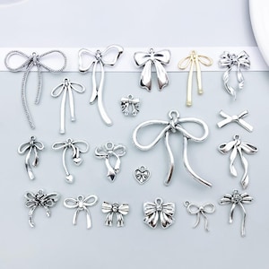 Peut inclure: Une collection de breloques en métal en forme de nœud dans des tons argentés et dorés. Ces petits pendentifs décoratifs présentent des motifs de rubans complexes, des boucles de fixation et des styles variés avec des extrémités tombantes.