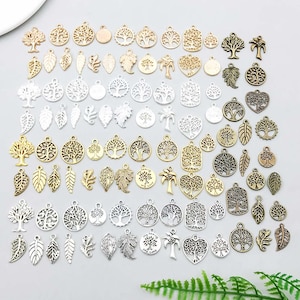 Op de afbeelding: Een verzameling diverse metalen bedels in goud, zilver en brons. De bedels tonen boom- en bladmotieven, waaronder openwerk boomhangers, effen boomvormen en bladsilhouetten. Ideaal voor het maken van sieraden en knutselprojecten.