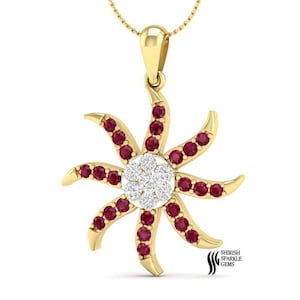 Puede incluir: Un collar con colgante de oro con un diseño de sol. El colgante tiene un grupo central de pequeñas piedras blancas rodeadas de piedras rojas. El diseño del sol es de oro y tiene una cadena delicada.