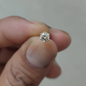 May include: A single stud earring featuring a round, faceted clear gemstone set in a six-prong silver-colored metal setting. The stone displays internal reflections and brilliance, held securely by the metal prongs in a classic solitaire design.