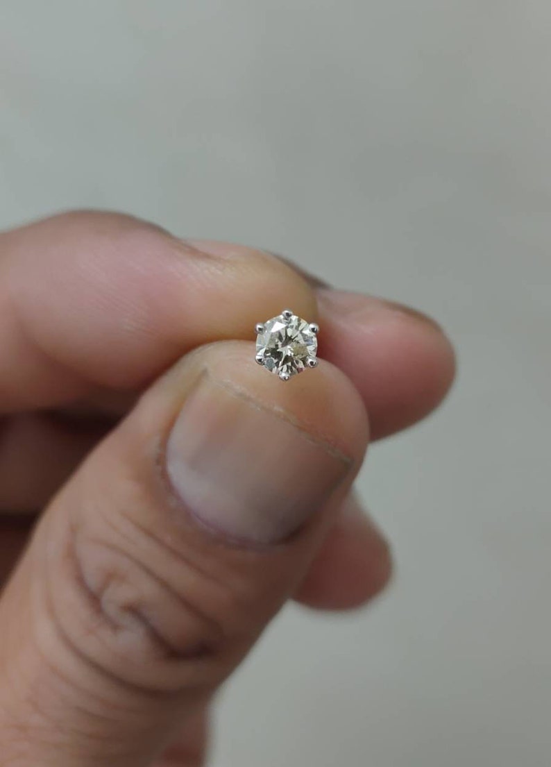 May include: A single stud earring featuring a round, faceted clear gemstone set in a six-prong silver-colored metal setting. The stone displays internal reflections and brilliance, held securely by the metal prongs in a classic solitaire design.