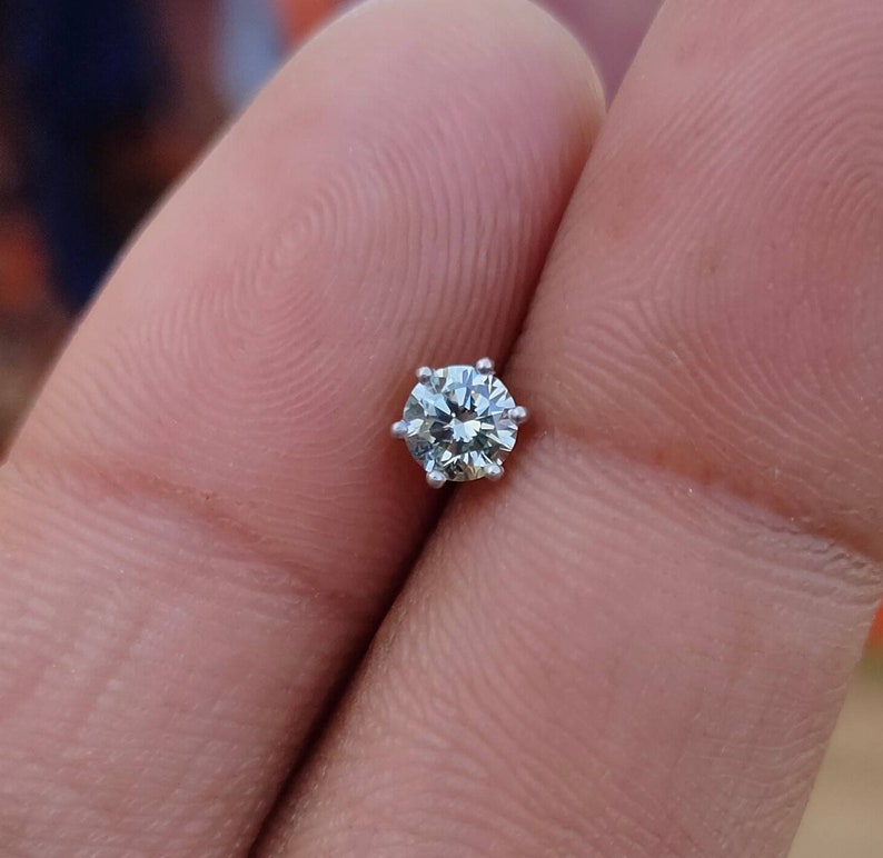 May include: A single round diamond gemstone set in a six-prong setting. The diamond is clear and sparkly.