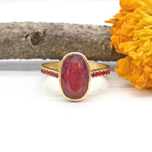 Può includere: Un anello d'oro con un grande rubino rosso ovale circondato da una fascia di rubini rossi più piccoli.