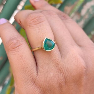 May include: A gold ring with a pear-shaped emerald green gemstone.