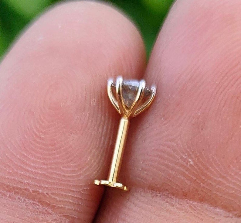 May include: A gold nose stud with a clear gemstone set in a prong setting.