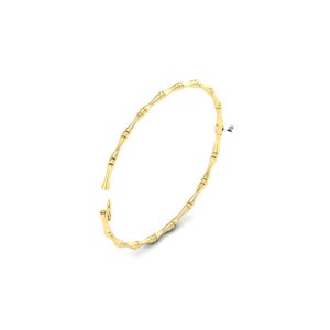 May include: A gold-colored bangle bracelet with a bamboo-inspired design. The bracelet is made of a shiny, metallic material and features a series of connected segments that mimic the look of bamboo stalks. The bracelet is open at one end, suggesting it is a hinged design.
